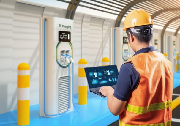 a man in a hard hat and safety vest holding a laptop fixing EV charger