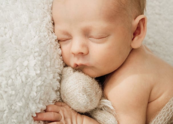 a newborn baby sleeping baby in a blanket and a teddy bear