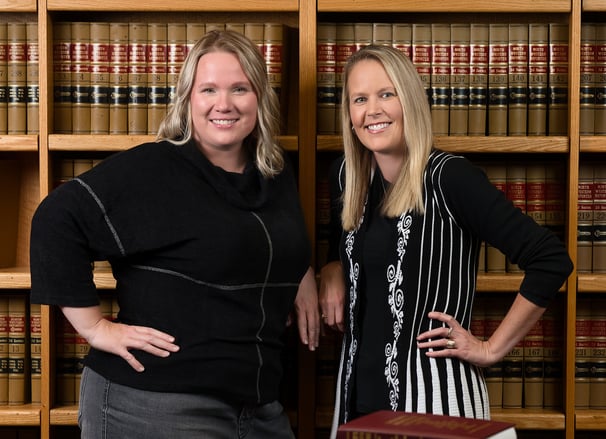 two women standing in front of a bookcase in an office