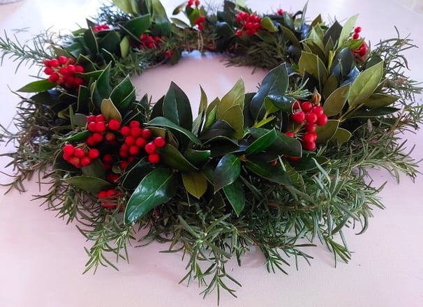 handmade rosemary holly berry and hineysuckle vine christmas wreath on a white tabletop