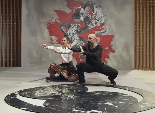 Ismet Himmet and Gizem Kara practicing a Tai Ji form on a yin-yang mat before a dragon mural.