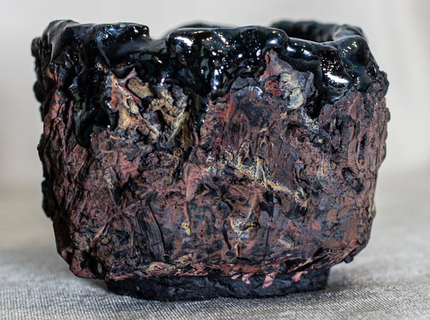 Raku-fired Kurinuki cup from Amman, Jordan, with black glaze, ochre tones, and volcanic textures