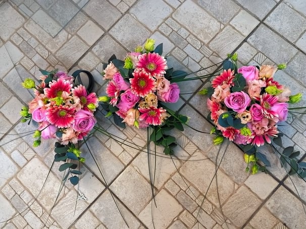 Trei buchete pastel cu trandafiri roz, gerbera și lisianthus, așezate pe podea cu model geometric.