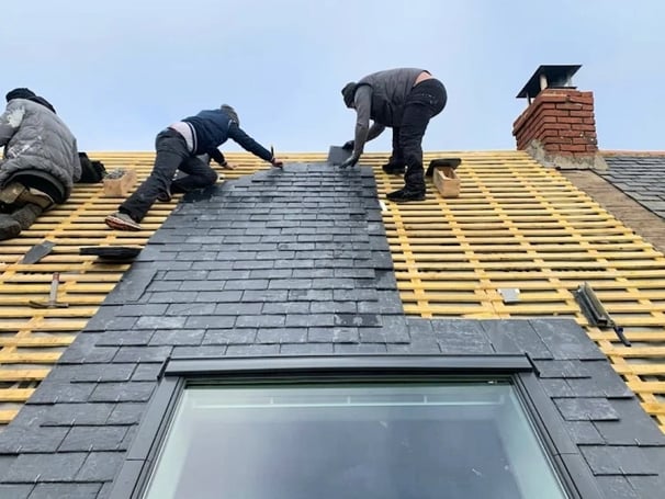 Trois couvreurs posant des ardoises sur charpente de toiture avec Velux
