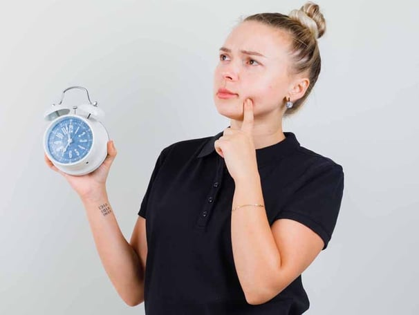 a woman holding a clock and looking at the time and thinking something