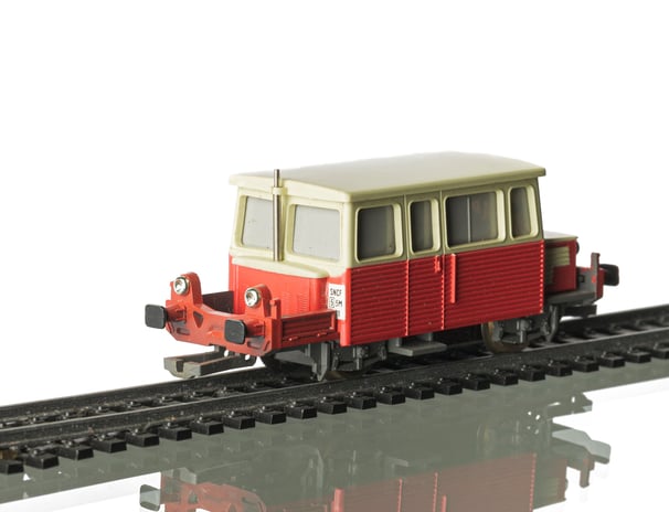 ancienne locomotive rouge et blanche de train miniature, sur rail, fond blanc avec reflet