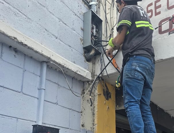 Instalación eléctrica en acometida de edificio por técnico con uniforme.