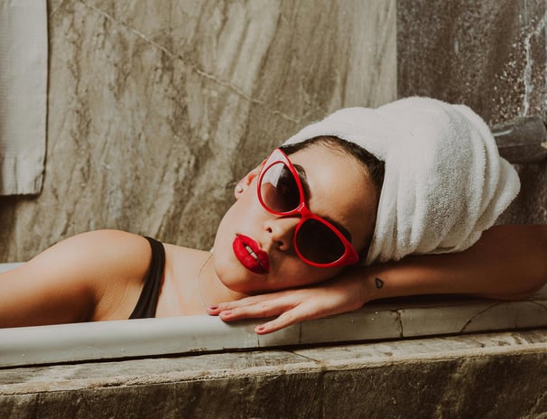 Modern woman in red sunglasses relaxing in bathtub with towel wrap — bold skincare ritual aesthetic