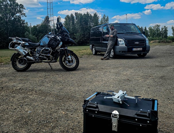 Dronekoffer, motorfiets en bestelwagen staan klaar voor drone-inspectie op locatie met lichtmast op de achtergrond