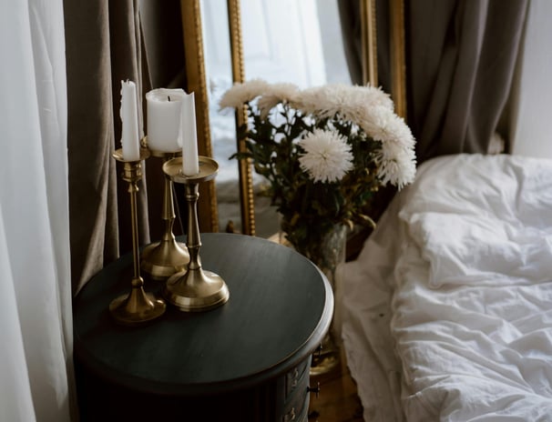 Moody bedside still life with gold candlesticks, mirror, and white flowers — romantic, vintage decor