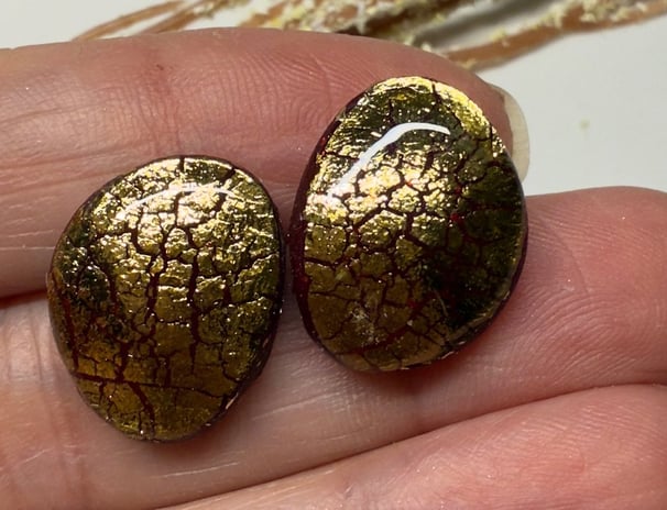 a person holding two gold earrings with gold foil