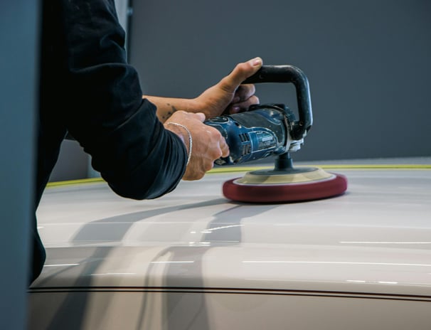 a person using a sander machine to polish a car- buffing a car at fix collision center