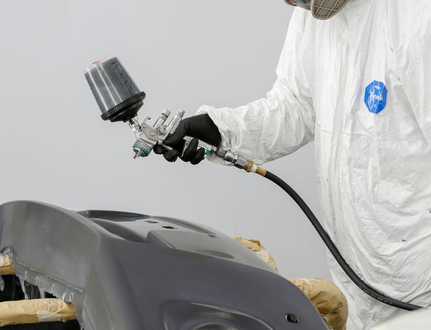 a man in a white suit and a white coat painting a car at fix collision center