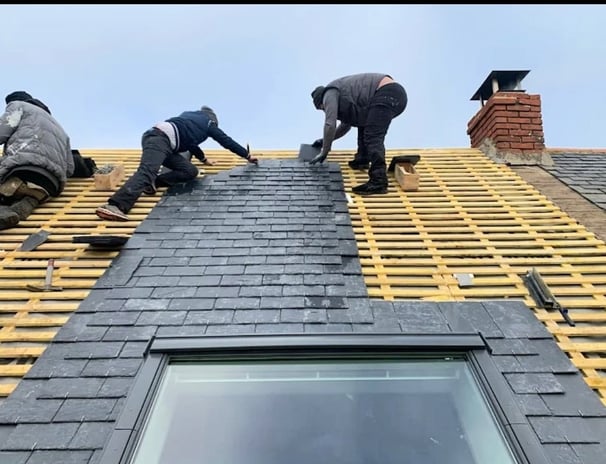 Trois couvreurs posant des ardoises sur charpente de toiture avec Velux
