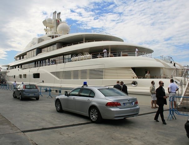 Security vehicle with flashing lights near a 130-meter luxury yacht in Italy, ensuring VIP safety.