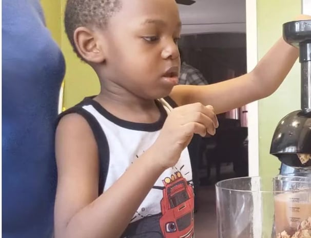 Child juicing fruit with patent supervising.