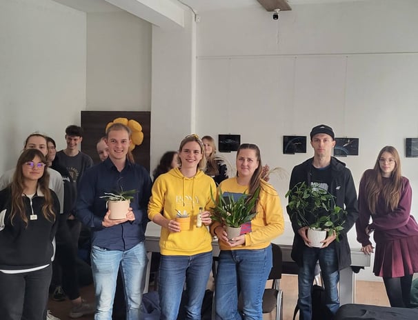 Orchidėjų laboratorijos renginio dalyviai sustoję kartu su lektore Vilte. Rankose laiko orchidėjas.
