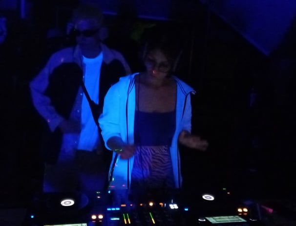 a woman in a white shirt and a man behind a DJ pult