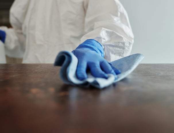 a person in a white lab coat and gloves cleaning a table