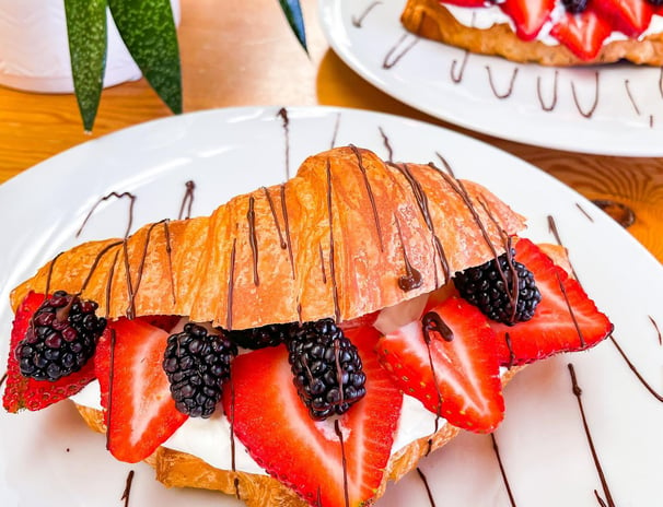 a croissant pastry with fruit on a plate with chocolate sauce