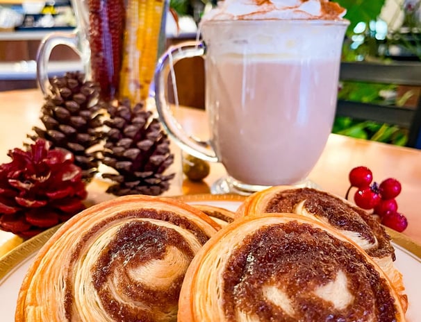 a plate with cinnamon roll pastry with a cup of strawberry tea latte