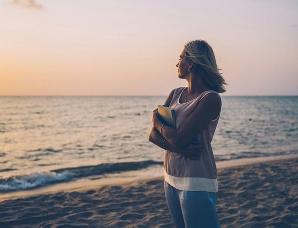 Mujer joven en la playa, abrazando un libro