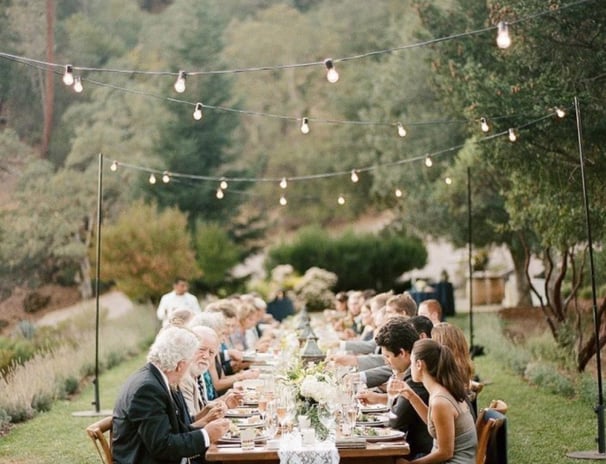 Dîner en plein air sous guirlandes lumineuses dans un jardin, longue tablée conviviale décorée