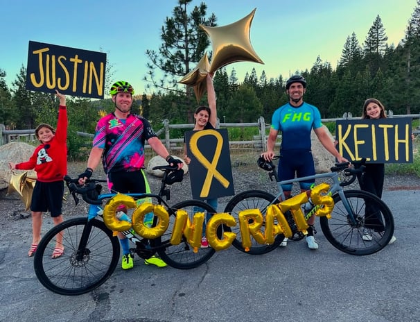 A group of people with balloons and a congrats sign with two cyclists