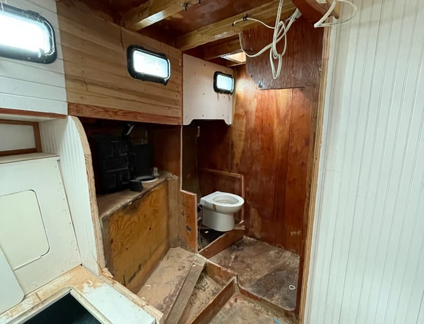 walls to the head (bathroom) cut open with a toilet perched in an unfinished wooden room
