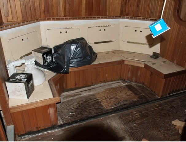 settee with some boat parts and a garbage bag on top in an unfinished interior made of wood