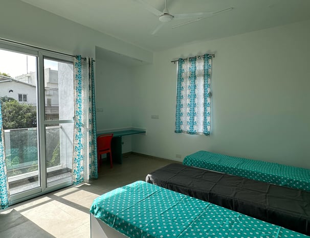 Spacious twin-sharing PG room in Banglore with a balcony, modern furniture, A/C and luxury.