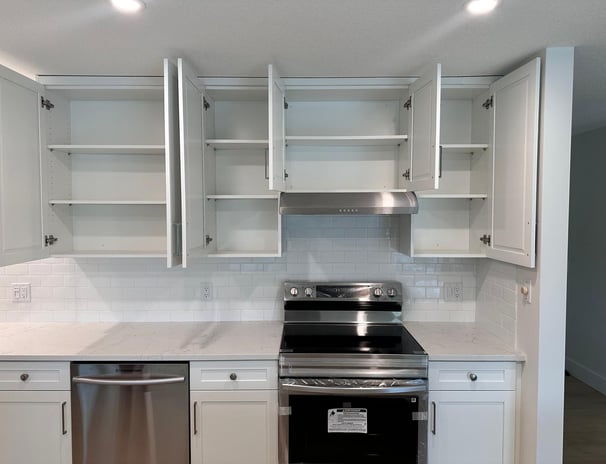 White shaker kitchen cabinets with open doors showing adjustable shelving, subway tile backsplash, q