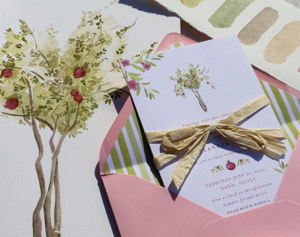close up of wedding invitation inside envelope with original pomegranate tree artwork in the back