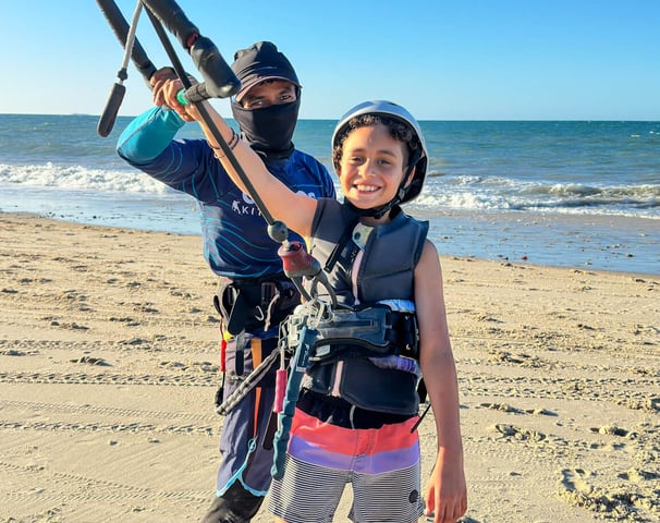 criança em pé na praia aprendendo kitesurf com o instrutor.