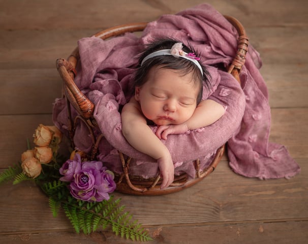 Una niña recién nacida durmiendo en una canasta con una flor en el cabello.