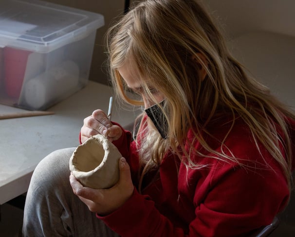 Young girl using a pencil tool to carve into a small ceramic cup.