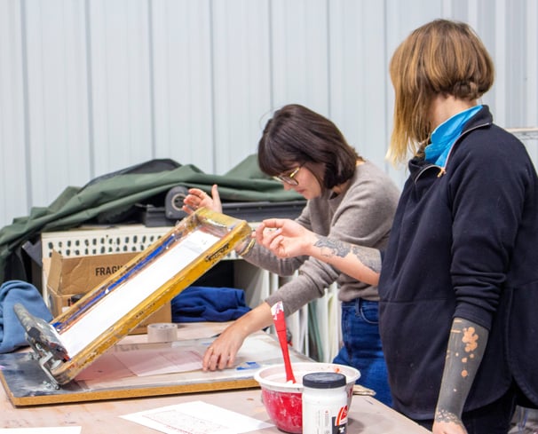 An instructor looking over a student aligning a paper under a screen.