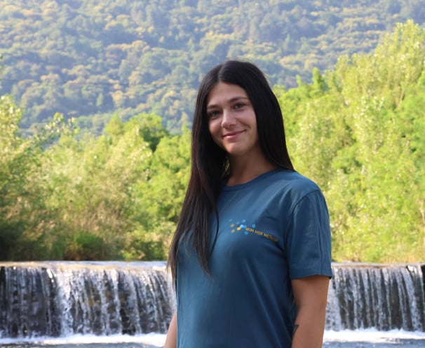 astrid mauri istruttrice certificata del metodo wim hof, davanti a una cascata con maglietta e logo 