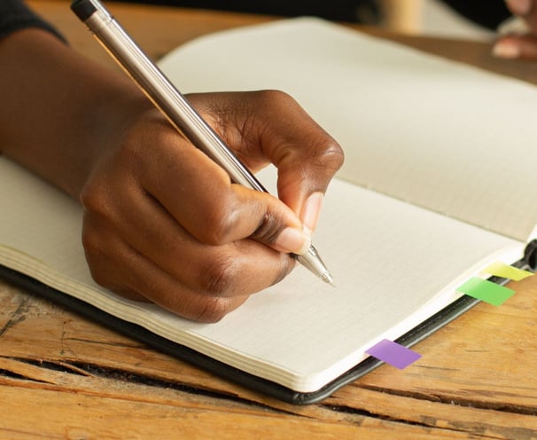 a person holding a pen and writing on a notebook