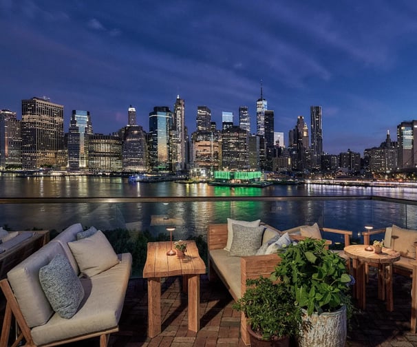 Rooftop lounge with view of New York City skyline at night.