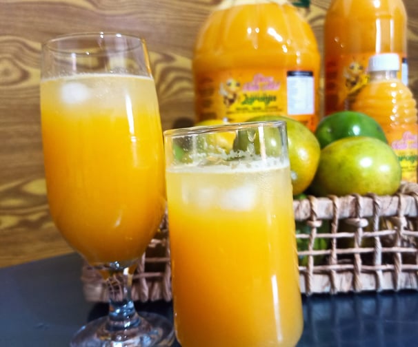 Uma taça sobre a mesa com saboroso suco laranja. E três garrafas de diferentes tamanhos de suco.