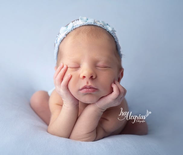 Una niña recién nacida durmiendo con las manos sobre la cabeza.