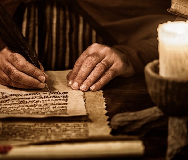 a man is writing a book on a table by a candle
