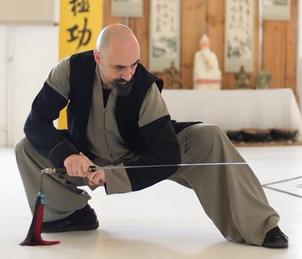 Ismet Himmet demonstrating a low Wudang sword stance (Jian) during indoor training with altar behind.