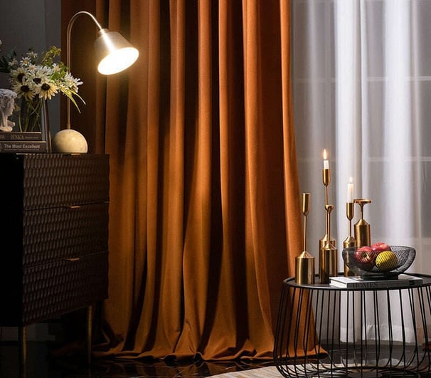 moody room, orange curtains, gold candles with a basked of fruit on black table, neutral curtains