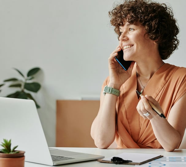 a woman sitting at a desk with a laptop and talking on a cell phone