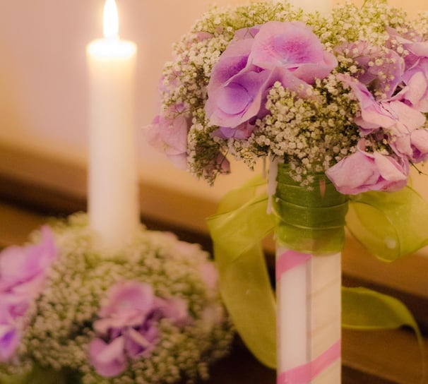 Lumânări de nuntă decorate cu hortensii mov și gypsophila, legate cu panglici verzi și roz.