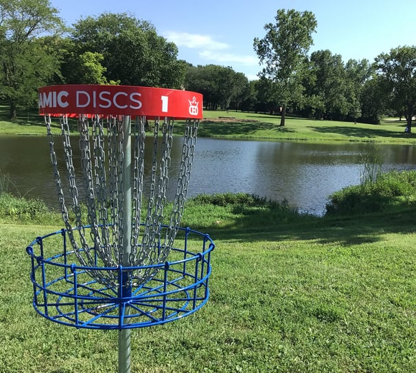 A disc golf basket in front of a pond.