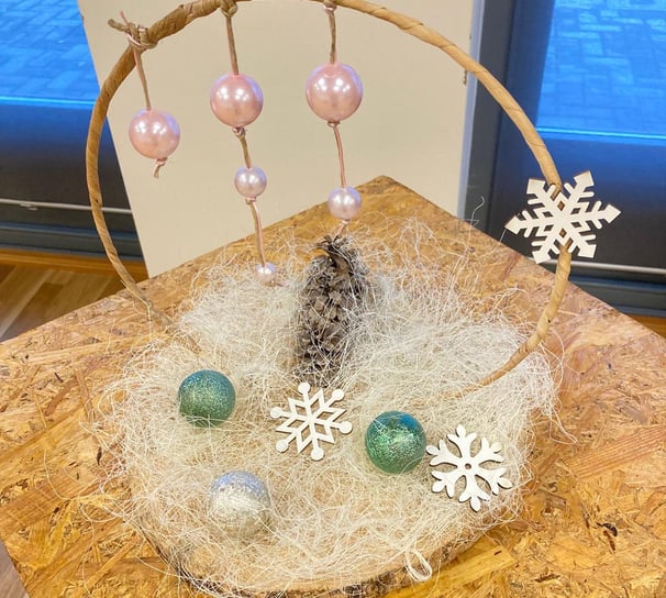 Decor de iarnă cu globuri roz și verzi, fulgi albi și con de brad, pe bază rustică din lemn.