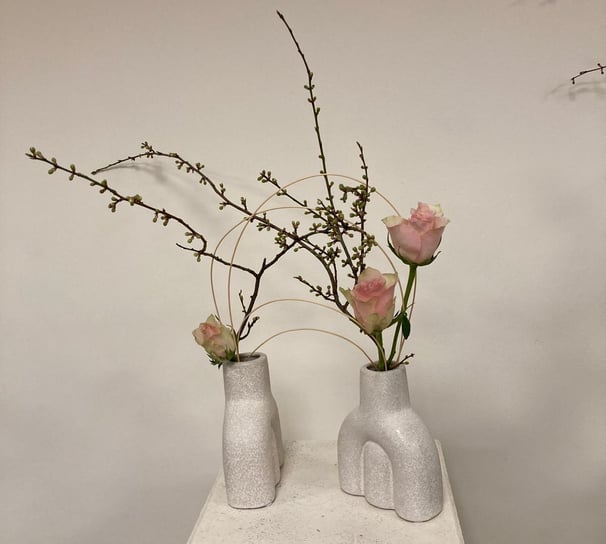 Ikebana modernă cu trandafiri roz și crenguțe, în vaze ceramice albe.